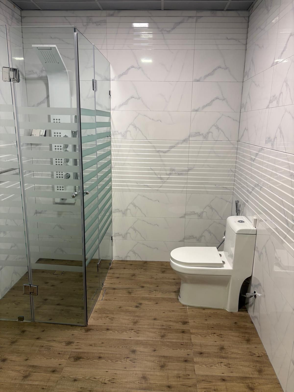 A bathroom with a glass shower enclosure, a toilet, and a wooden floor.