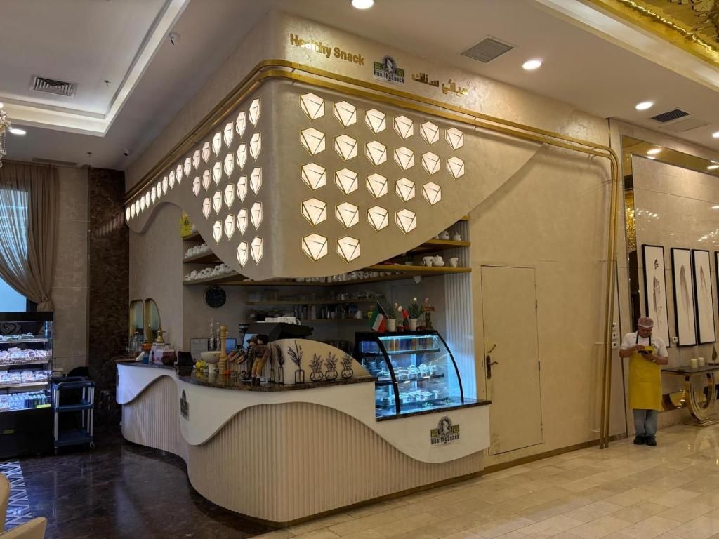Zona de recepción de hotel con mostrador, una pared de formas geométricas iluminadas y una persona de pie junto al mostrador.
