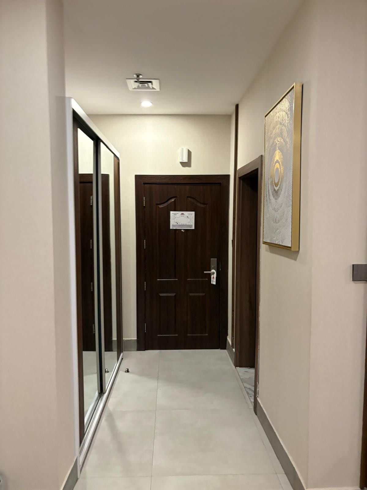 A hallway with a wooden door at the end, a framed artwork on the wall, and a ceiling light fixture.