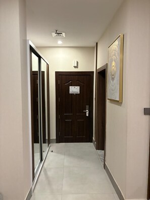 Un pasillo con una puerta de madera al final, una obra enmarcada en la pared y una lámpara en el techo.