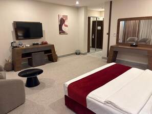 A hotel room with a bed, a desk, a television, and a mirror. - Garden Hotel (Jabriya)