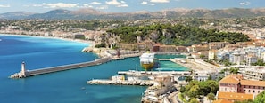 A coastal city with a prominent lighthouse, a large cruise ship docked at a marina, and a mix of residential and commercial buildings. - Studio à louer Carré d'Or à Nice (Nice)