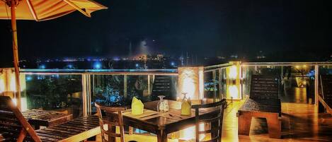 A wooden deck with a table and chairs, a large umbrella, and a view of the city at night.
