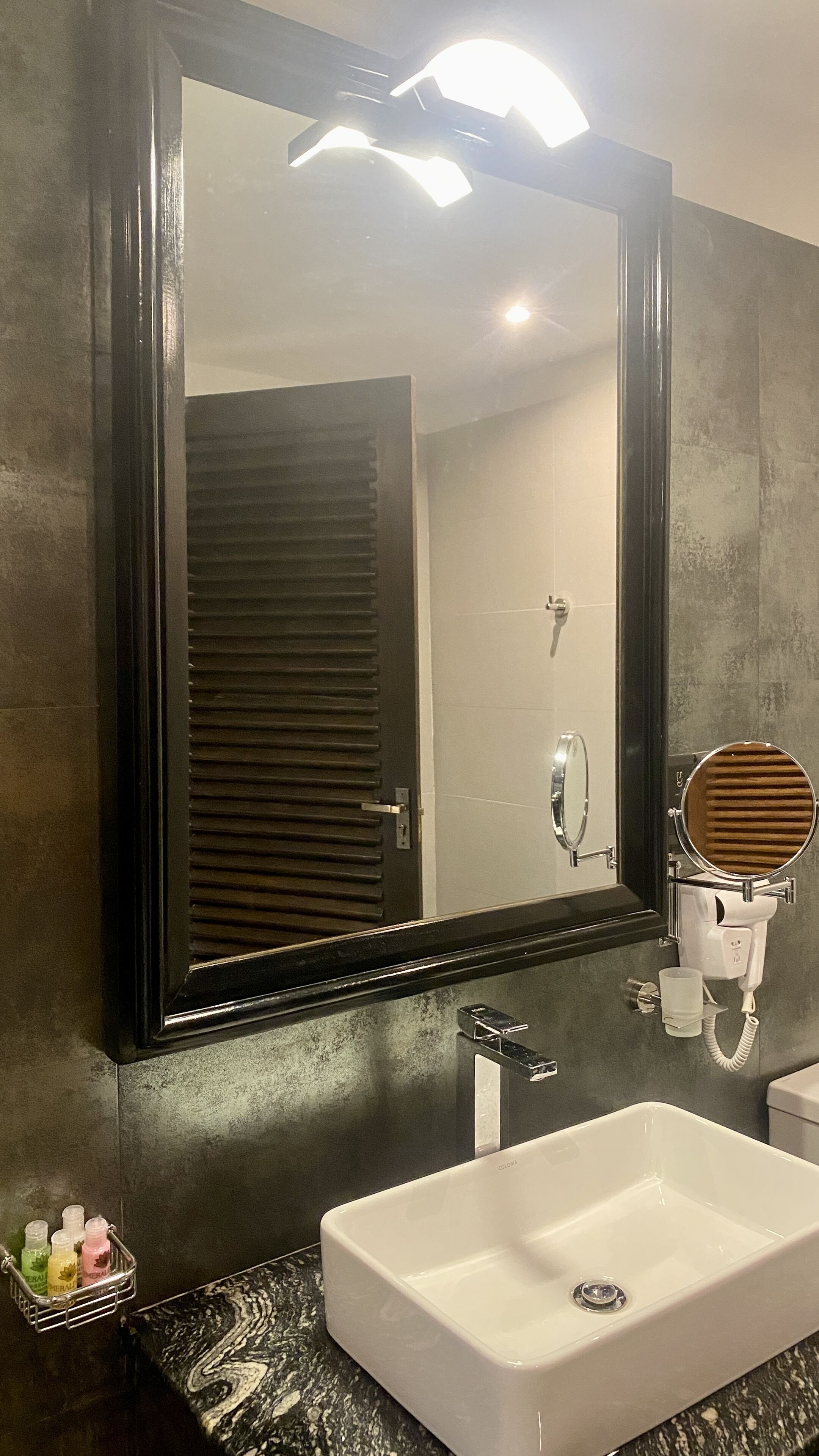 A bathroom with a large mirror, a white sink, and a hairdryer mounted on the wall.