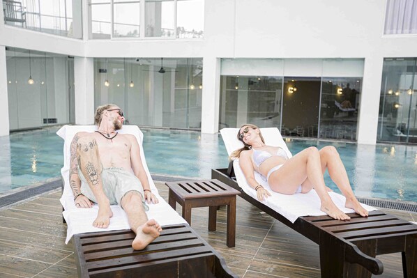 Two people relaxing by a poolside lounge area with a view of the pool and a building in the background. - Emerald Bay Resort Mirissa (Mirissa)