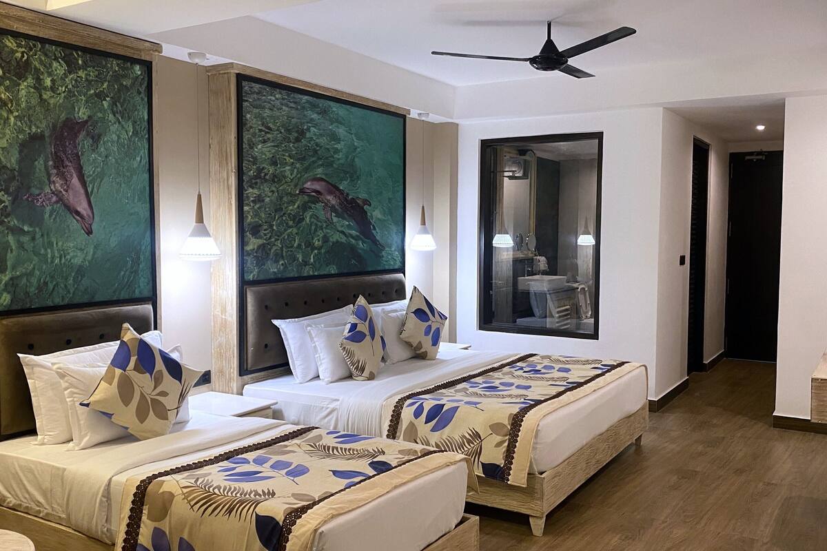 A hotel room with two beds, a large mirror, a ceiling fan, and a painting of a forest scene.