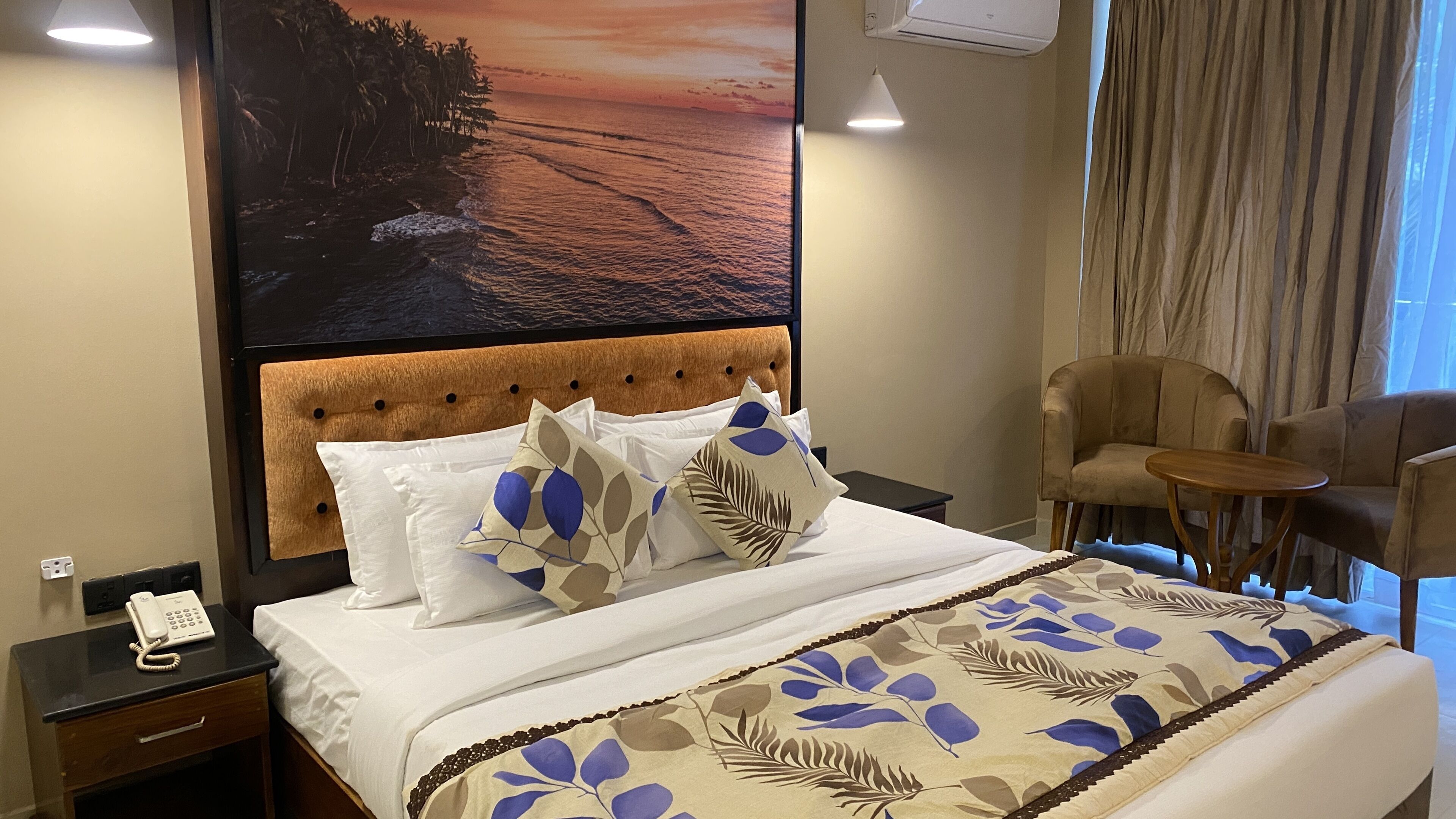 A hotel room with a bed, a nightstand with a phone, a chair, and a view of the ocean.