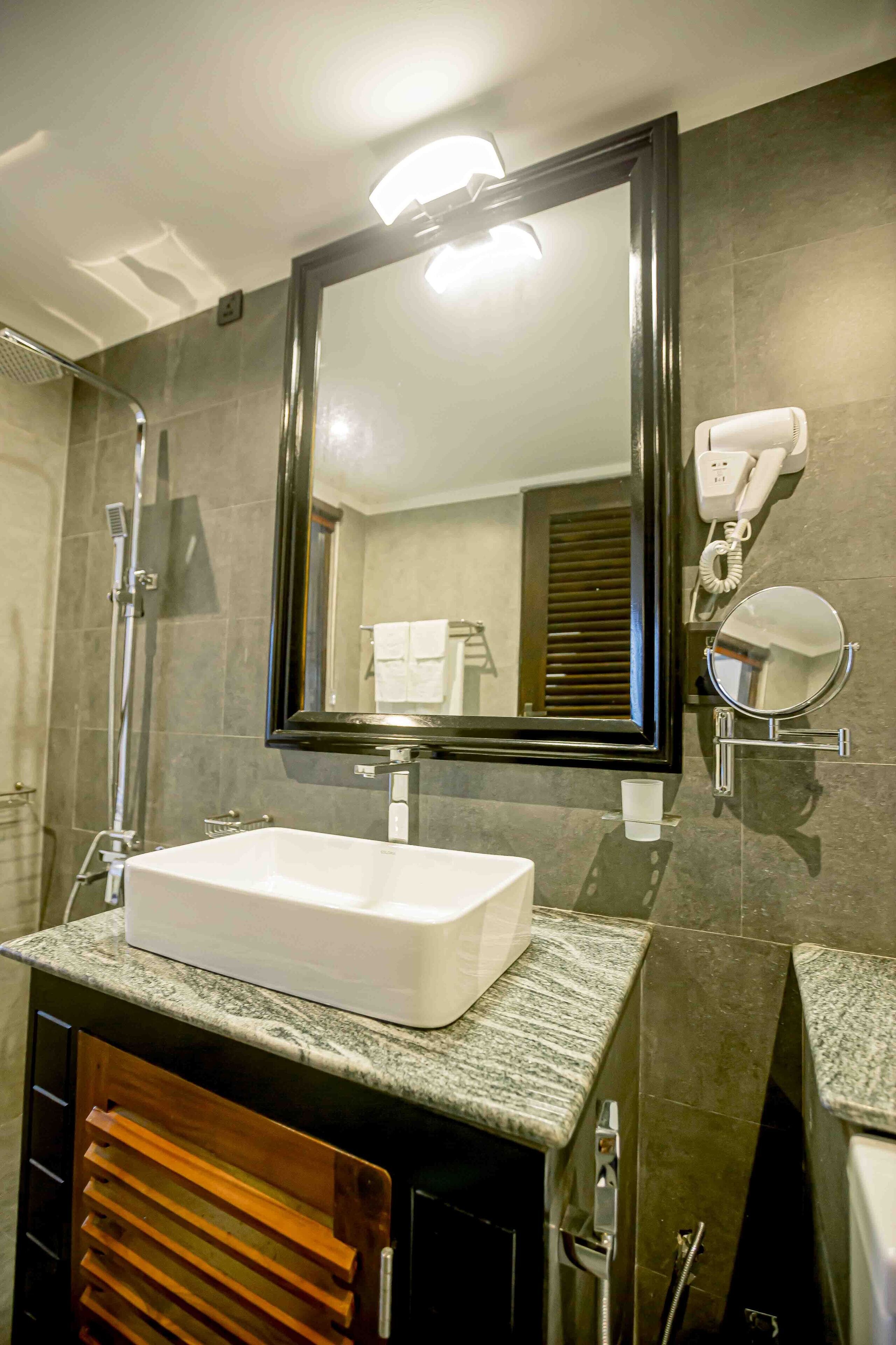 Un baño con un lavabo rectangular, un espejo grande, un secador de pelo portátil y un cabezal de ducha.