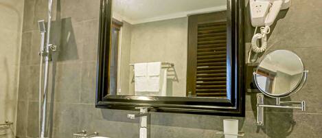 Un baño con un lavabo rectangular, un espejo grande, un secador de pelo portátil y un cabezal de ducha.