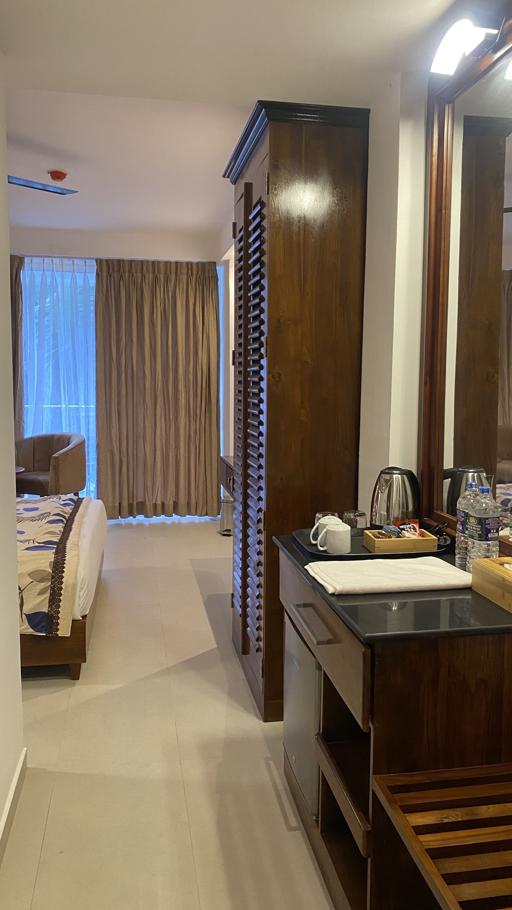 Una habitación de hotel con una cama, un escritorio con tetera y tazas, un espejo y un armario.