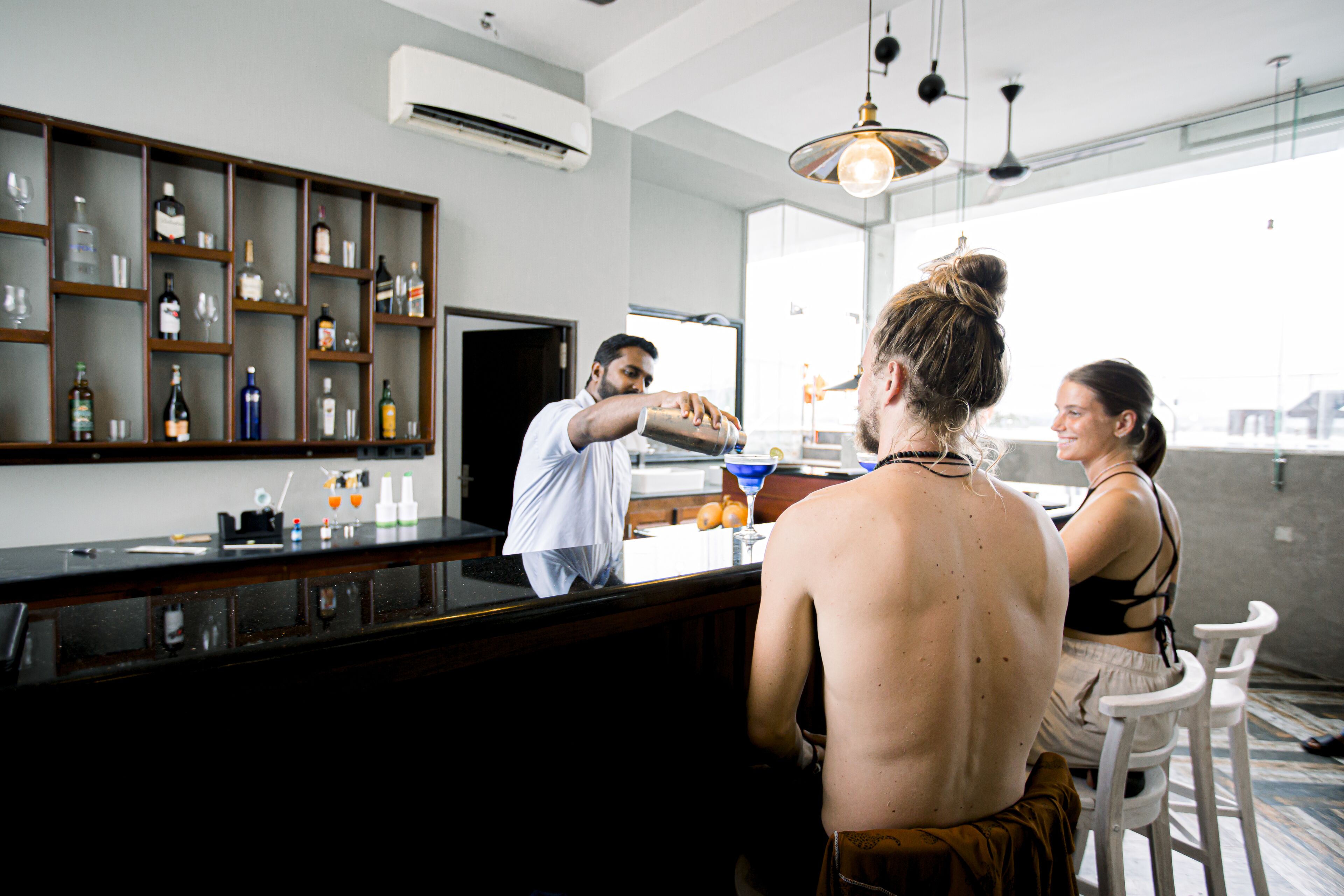 A bar area with shelves of bottles and glasses, a counter, and a person pouring a drink.