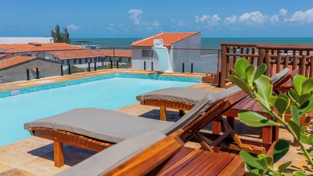 Zona de piscina con sillones de descanso y un tobogán, con vistas al mar azul y transparente.