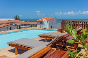 A pool area with lounge chairs and a water slide, overlooking a clear blue sea. - Pousada Rota do Kite Preá (Cruz)