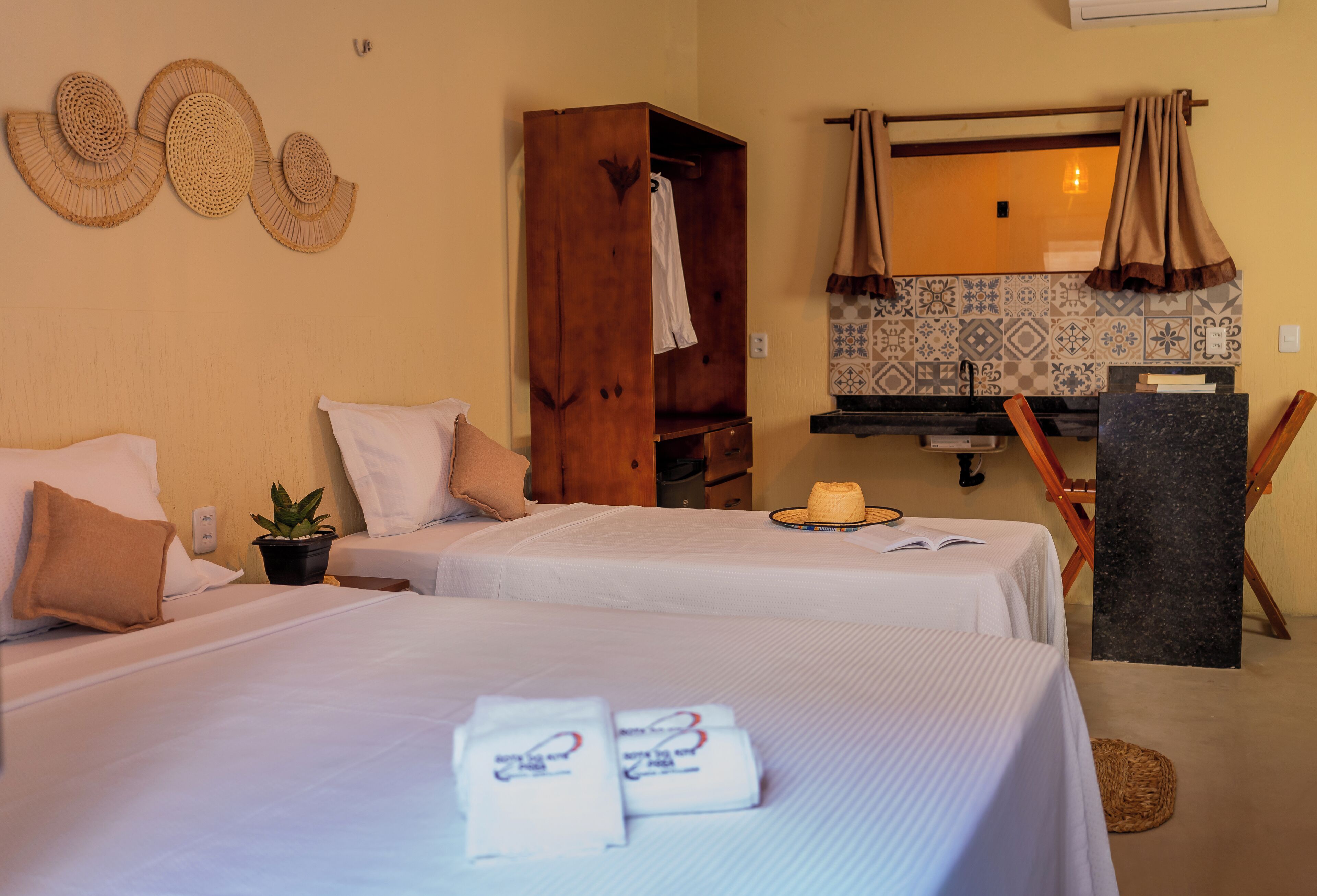 A hotel room with two beds, a wooden wardrobe, a mirror, a towel rack, and a small potted plant.