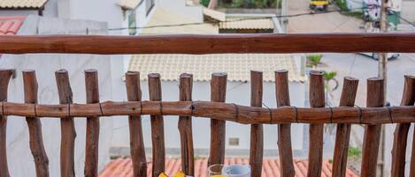 Una mesa de madera con desayuno, incluyendo pan, fruta y bebidas, en un balcón con vistas al mar.