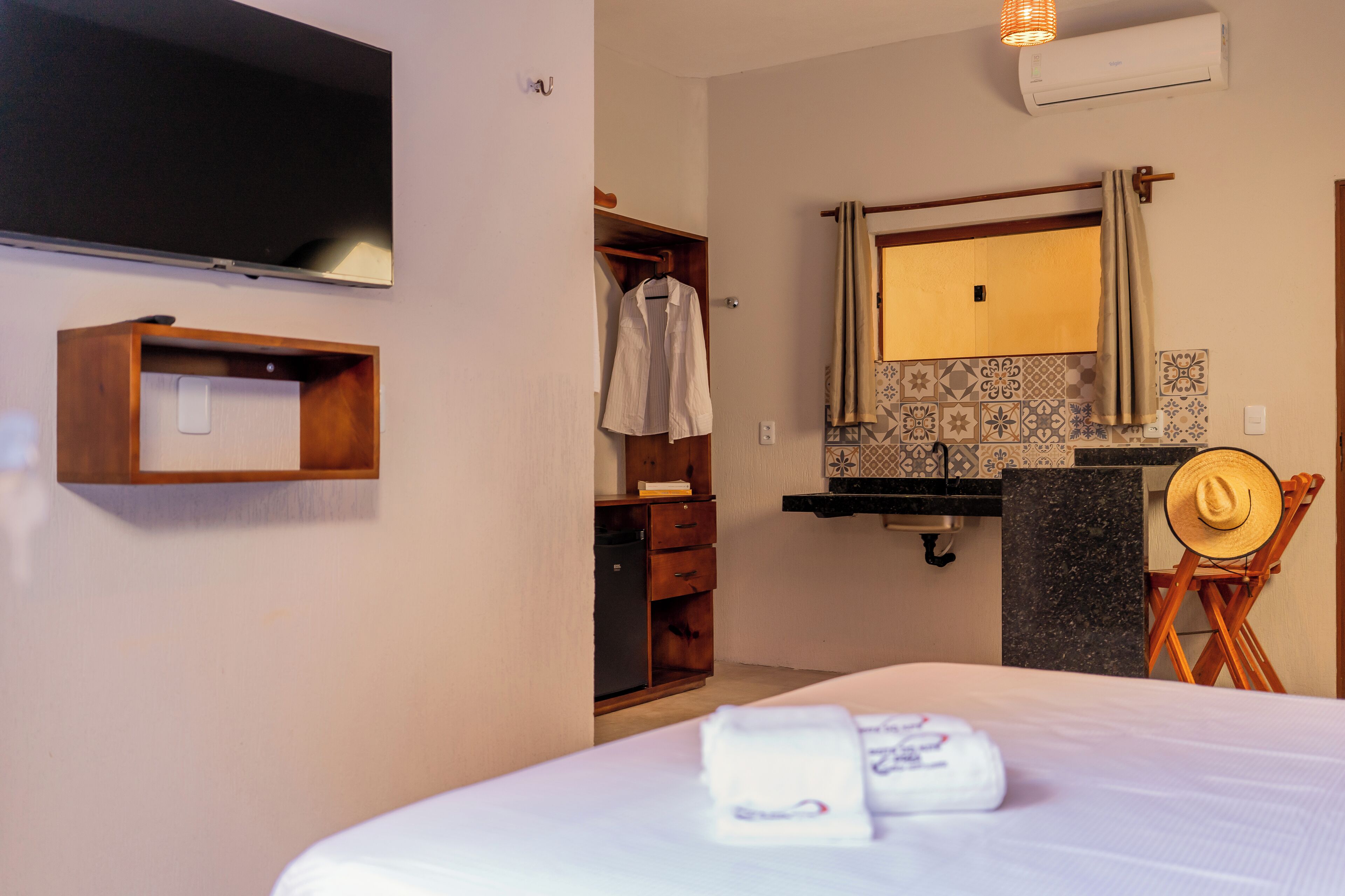 A hotel room with a bed, a TV, a wooden wardrobe, a bathroom with a mirror, and a towel on the bed.