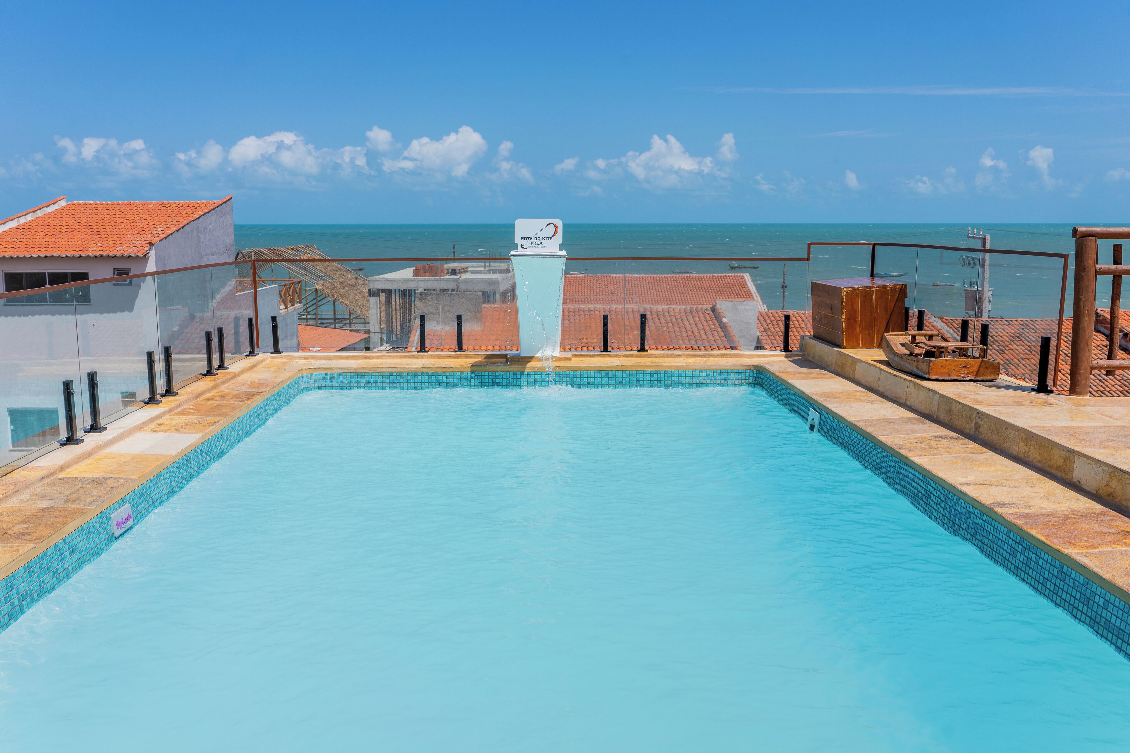A swimming pool with a view of the ocean, a sign indicating a hotel, and a tiled roof structure.