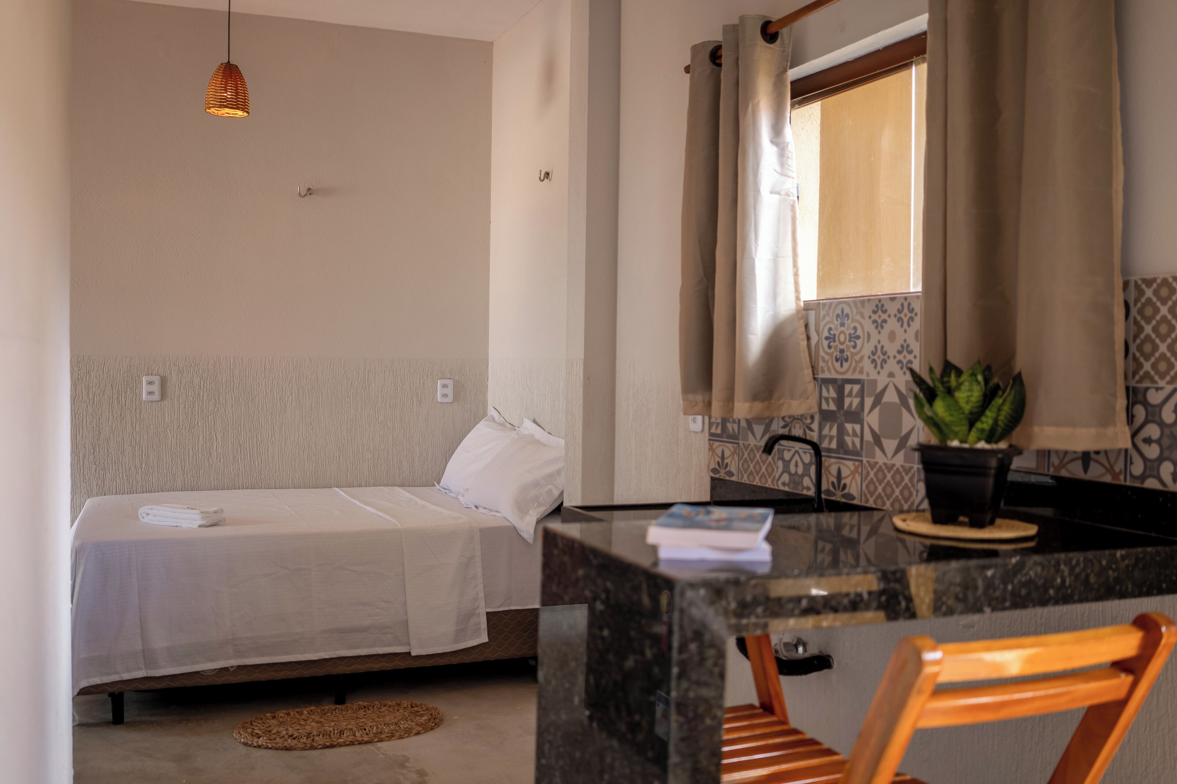 A compact room with a bed, a small kitchen area with a sink and a potted plant, and a dining table with chairs.