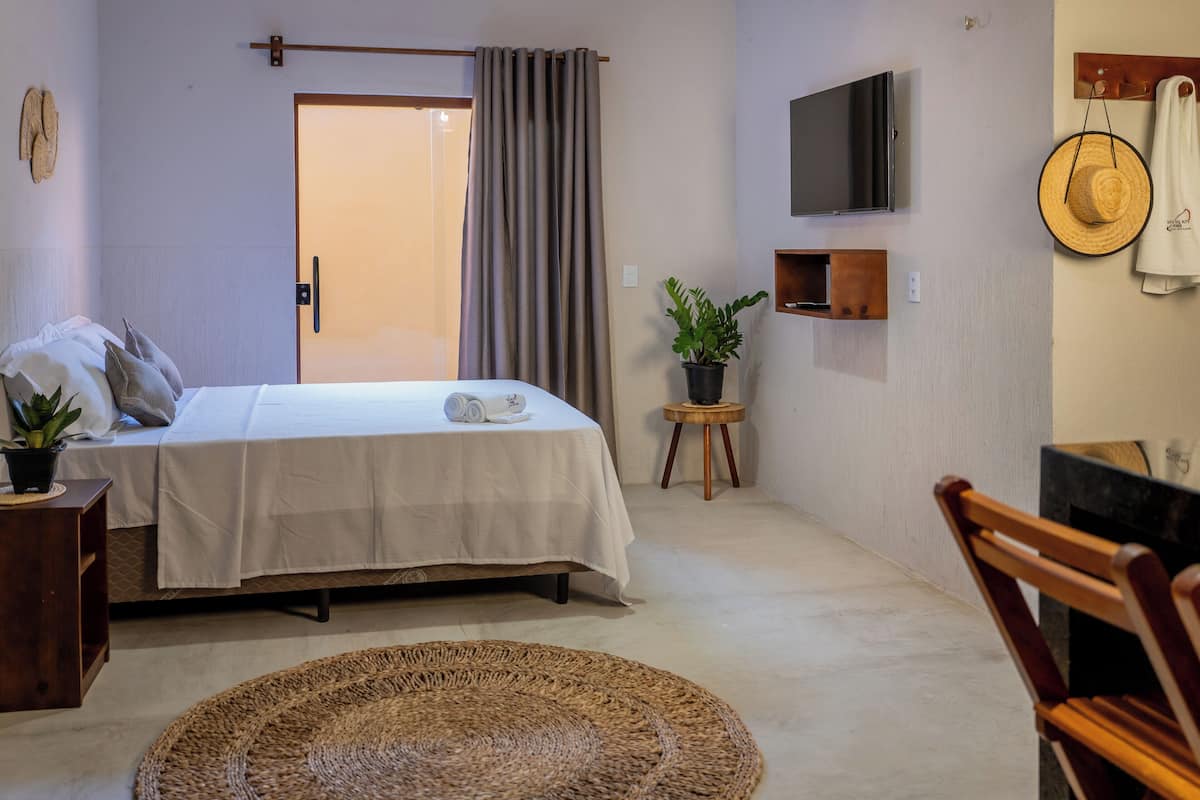 A bedroom with a bed, a TV, a potted plant, a wooden chair, and a round woven rug.
