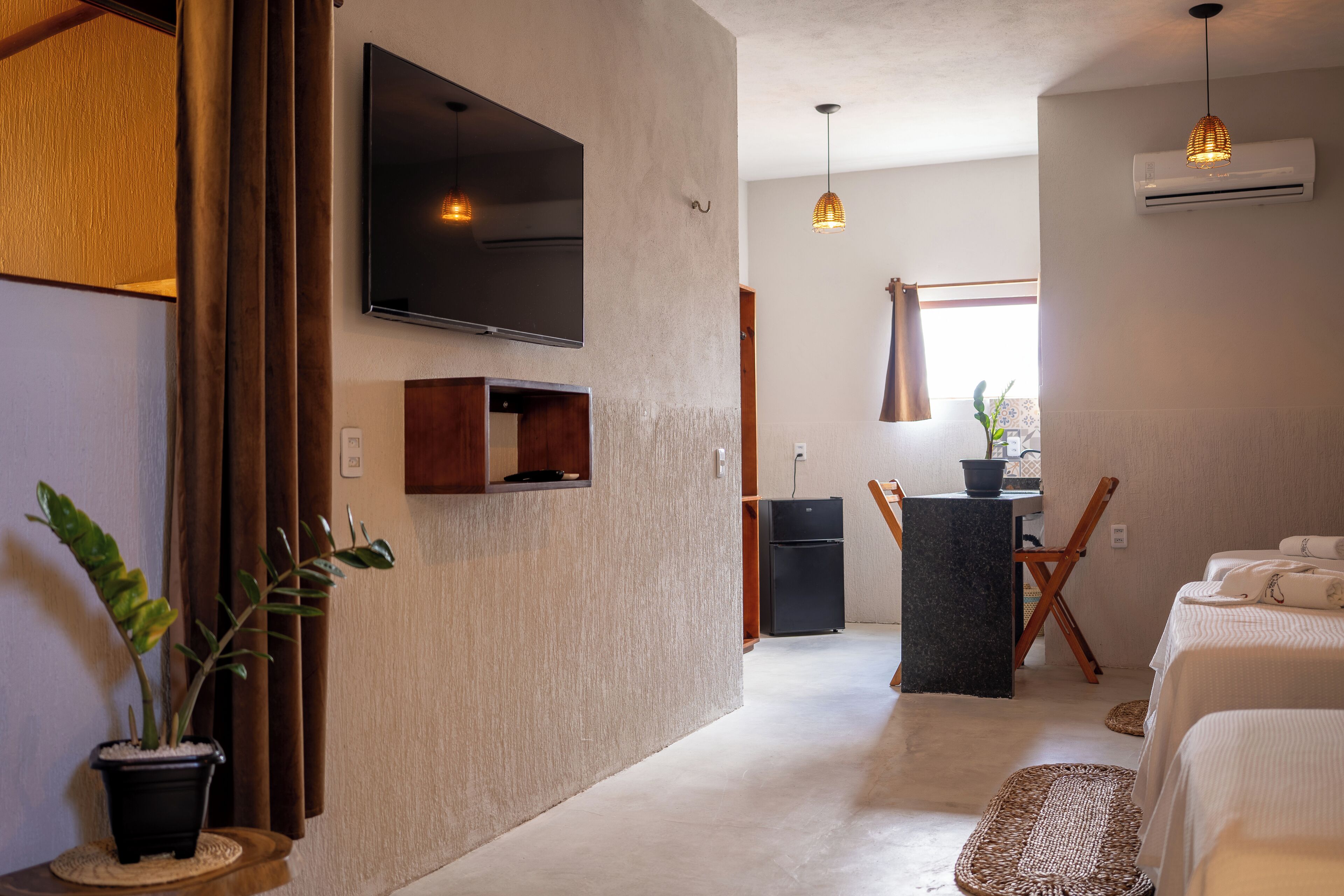 A modern living room with a flat-screen TV, a dining area with a table and chairs, and a kitchen area with a refrigerator.