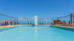 A clear blue pool with a central fountain, surrounded by a glass enclosure and a wooden deck.