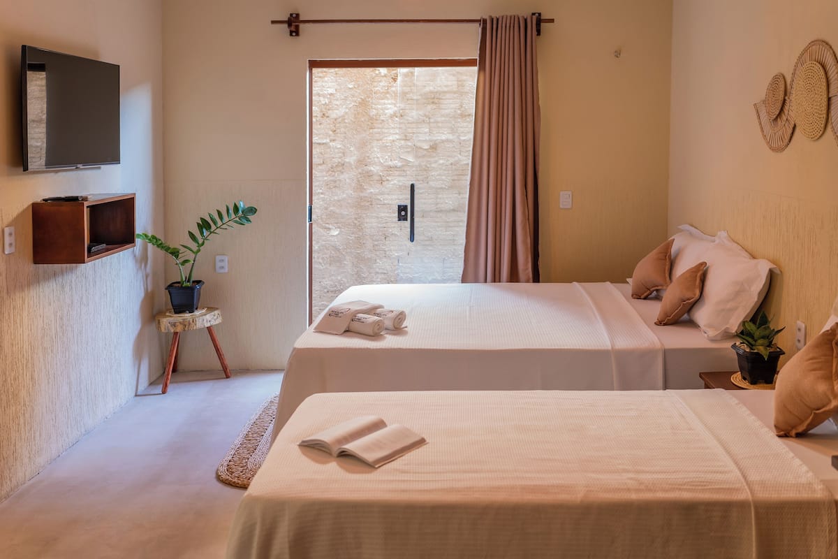 A hotel room with two beds, a TV, a small table with a plant, and a view through a door.