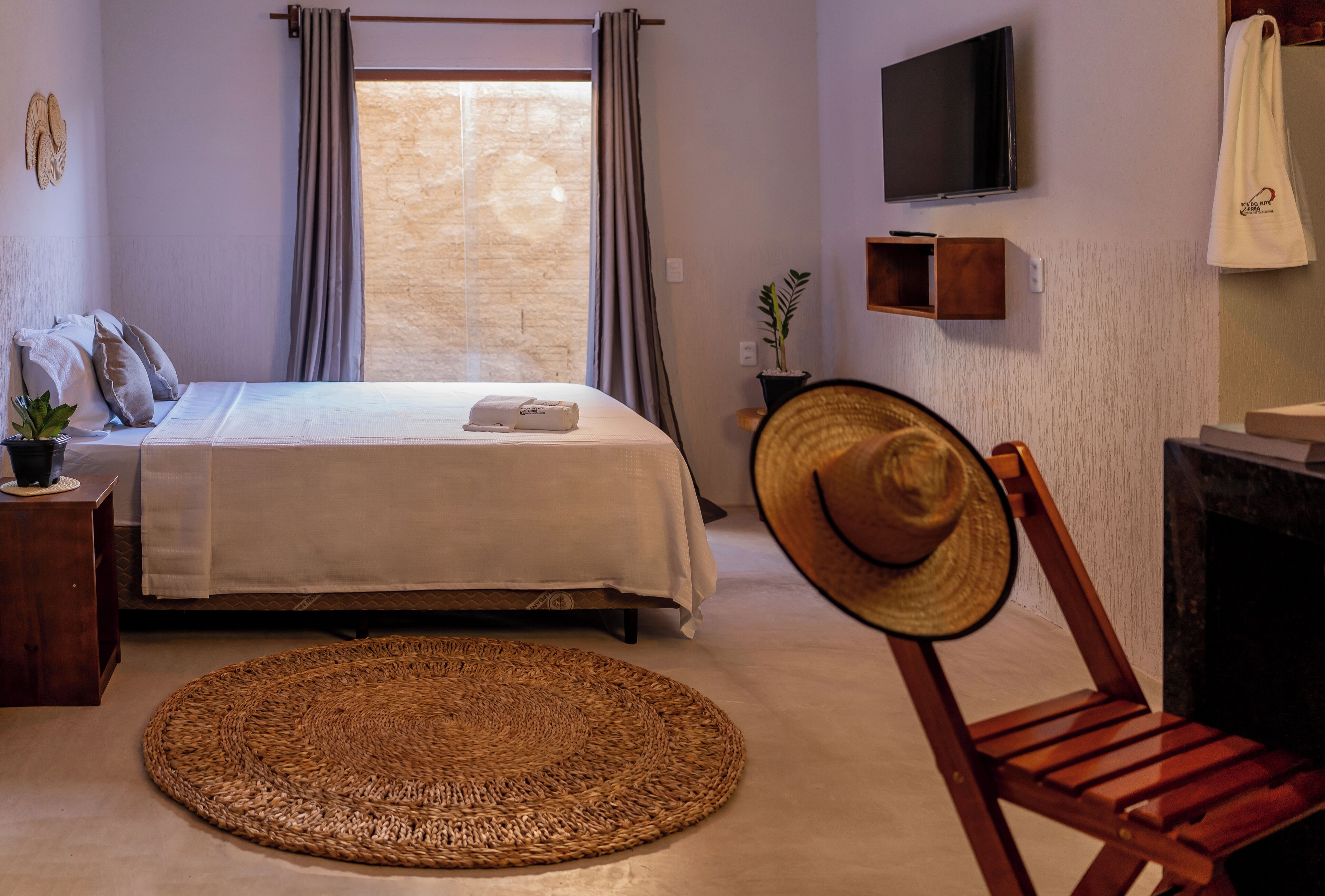 A bedroom with a bed, a round woven rug, a wooden chair, a TV, and a small shelf.