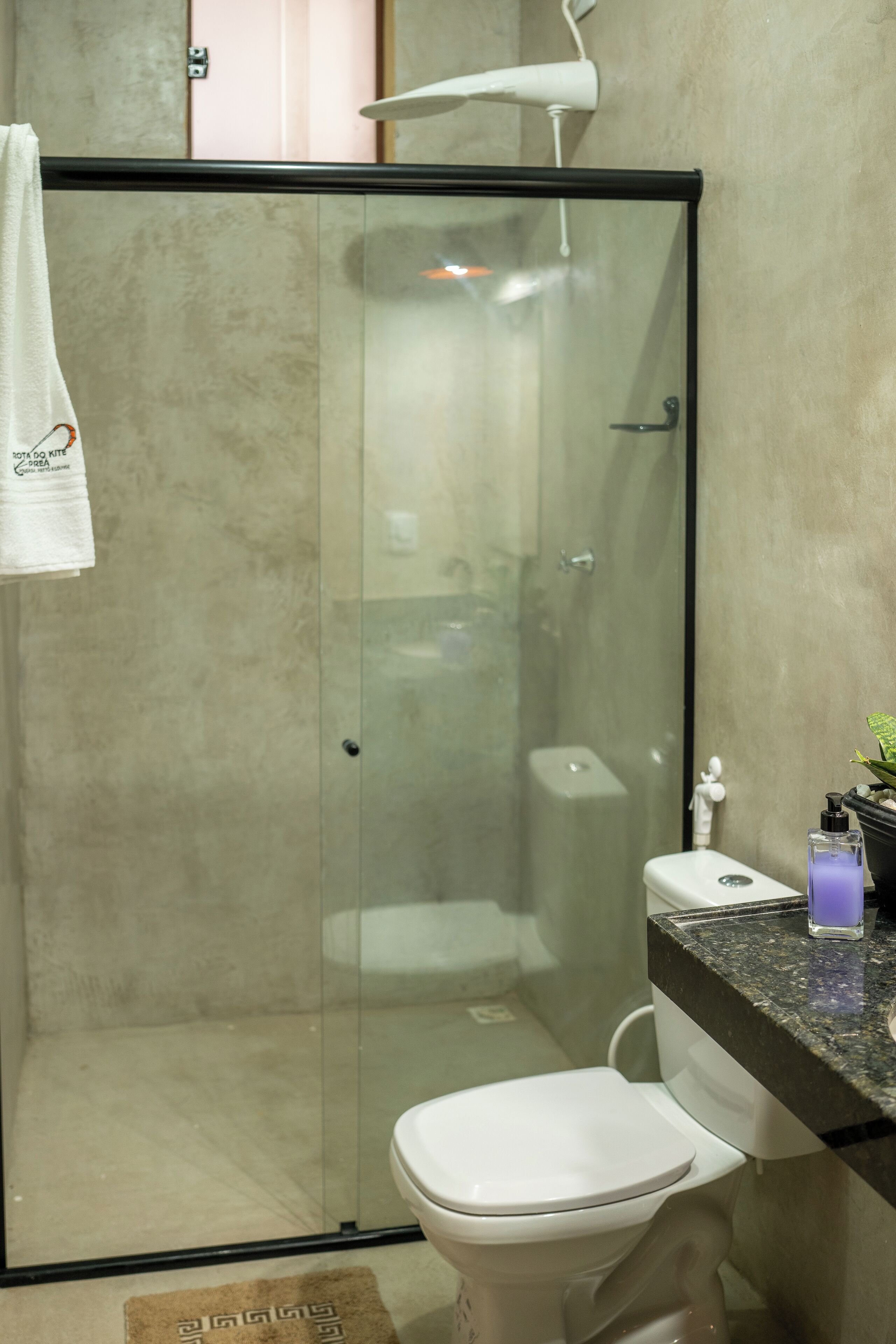 A modern bathroom with a glass-enclosed shower, a white toilet, and a granite countertop with toiletries.