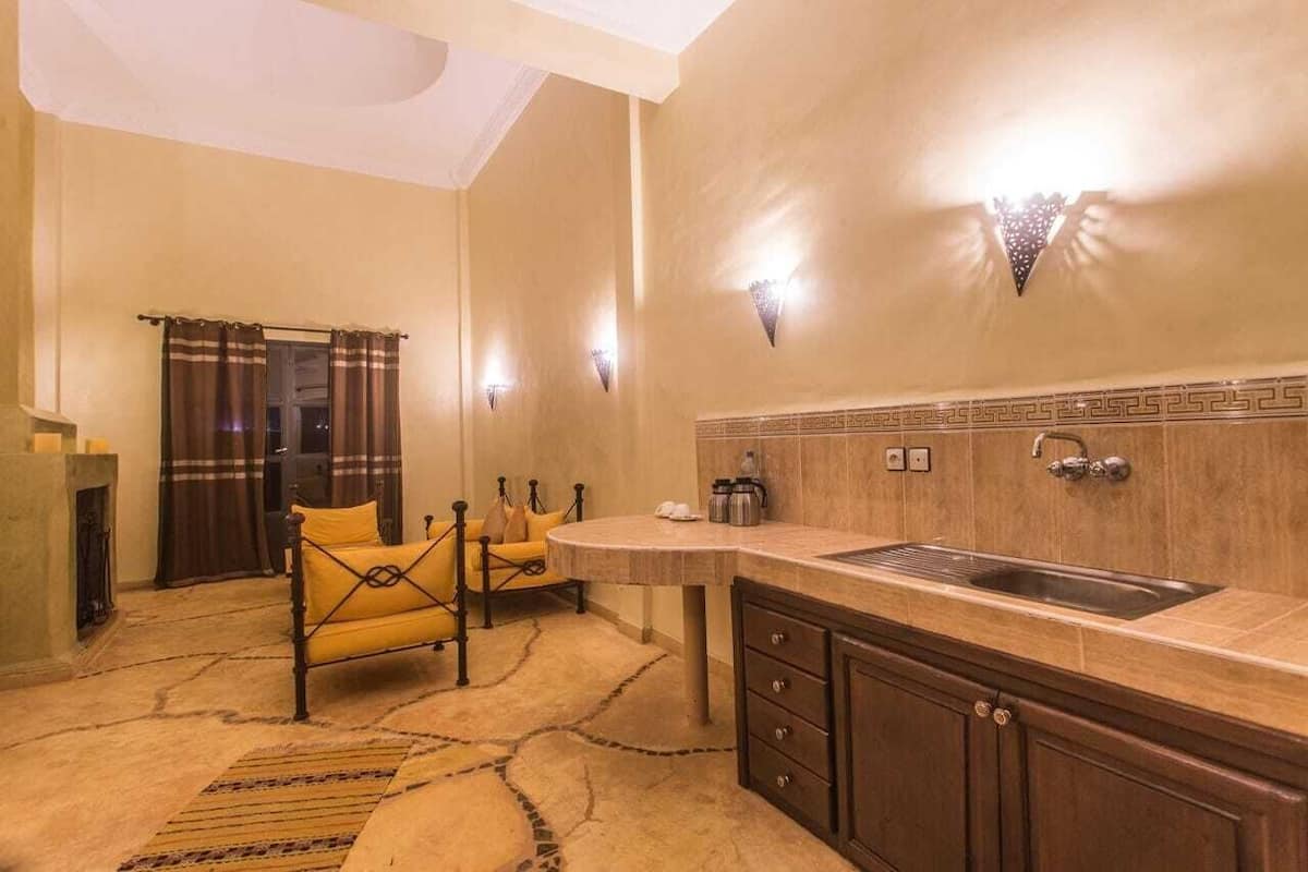 A compact kitchen with a sink, a small dining area with a yellow chair, and a decorative wall with light fixtures.