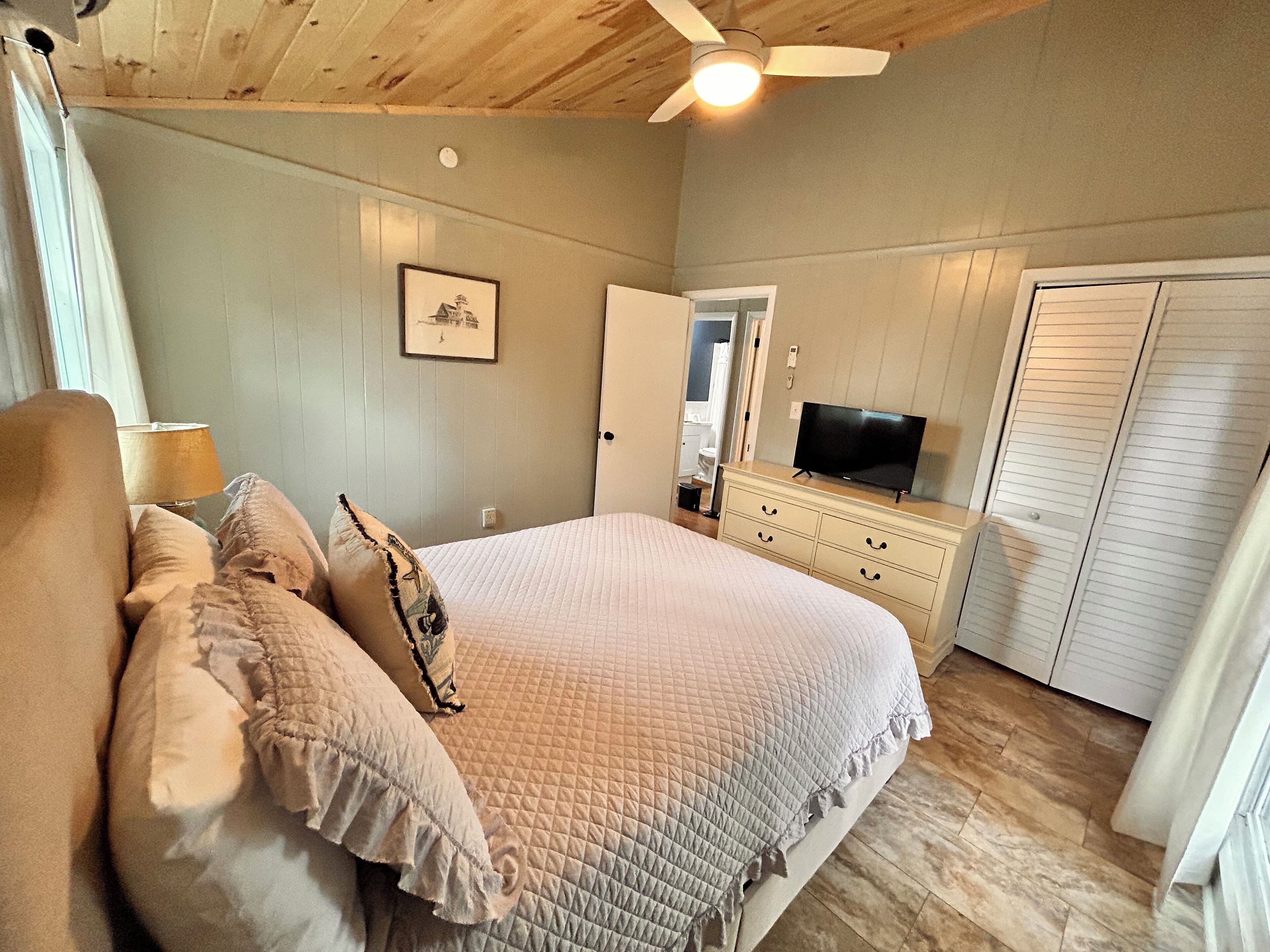 A bedroom with a bed, a dresser, a television, and a ceiling fan.