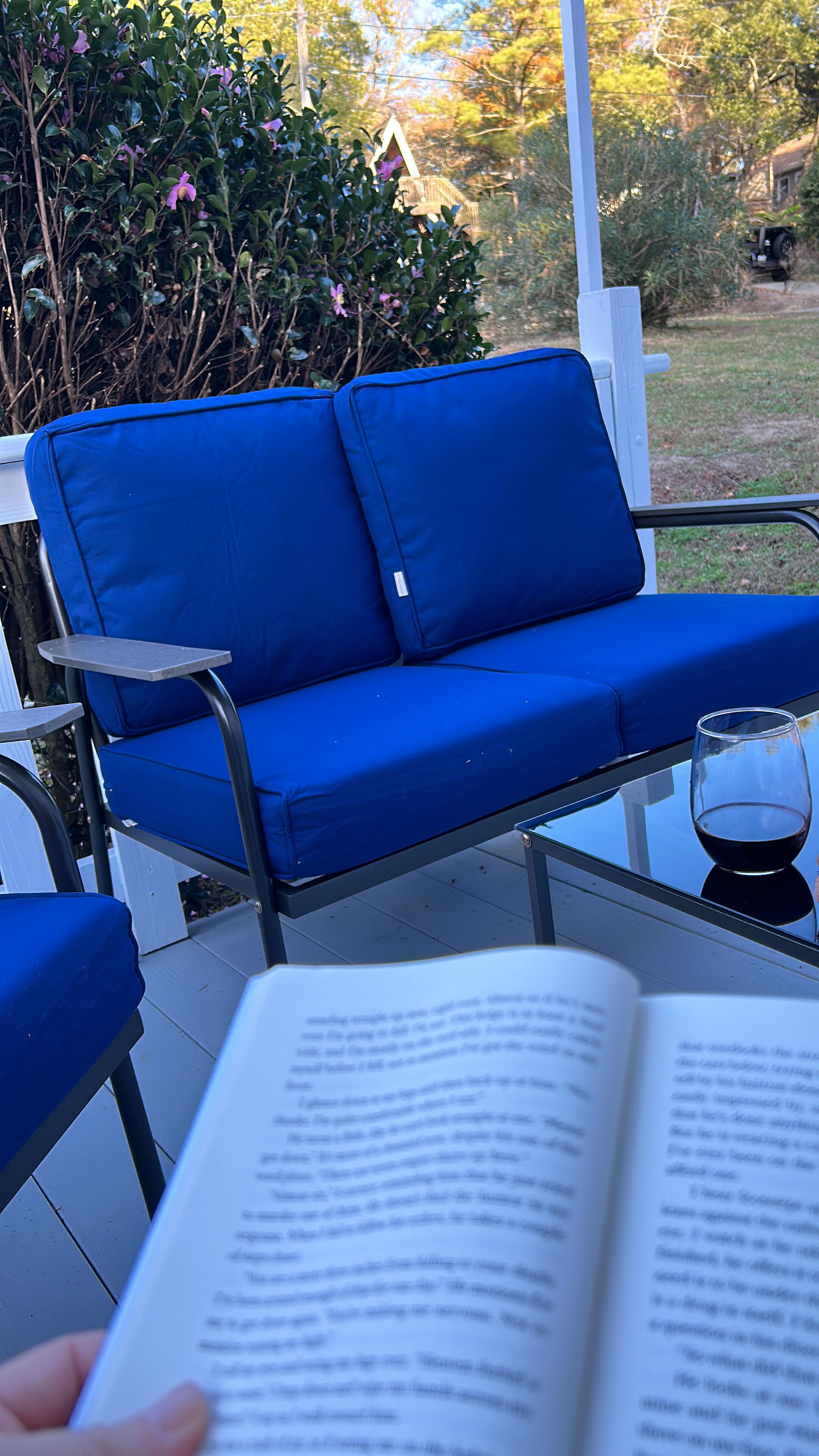Een blauwe zitplek buiten met een glazen tafel en een boek.