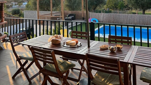 Ein überdachter Essbereich im Freien mit Tisch für vier Personen, mit Blick auf einen Swimmingpool und die umliegende Landschaft.