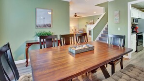 Un comedor con una mesa de madera, sillas y un ventilador de techo. Se ve una escalera que sube a otro nivel.
