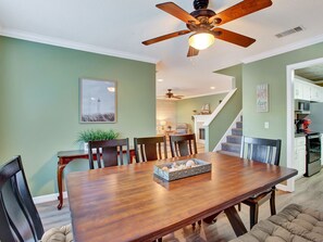 Un coin repas avec une table en bois, des chaises et un ventilateur de plafond. Un escalier mène à un autre niveau.