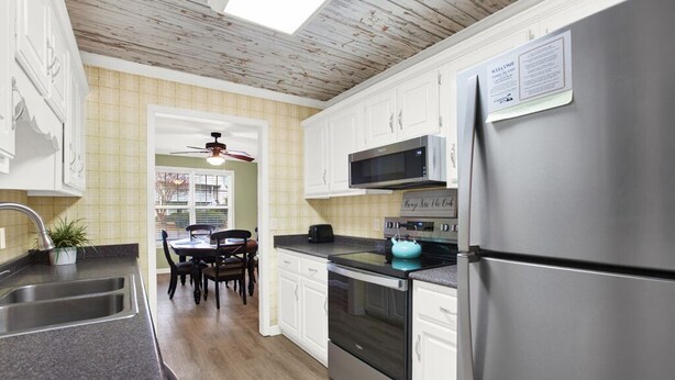 Una cocina moderna con armarios blancos, electrodomésticos de acero inoxidable y una zona de comedor con mesa y sillas.