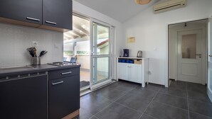 A modern kitchen with dark cabinets, a countertop, and a sliding glass door leading to a balcony. - Apartments Domic (Medulin)