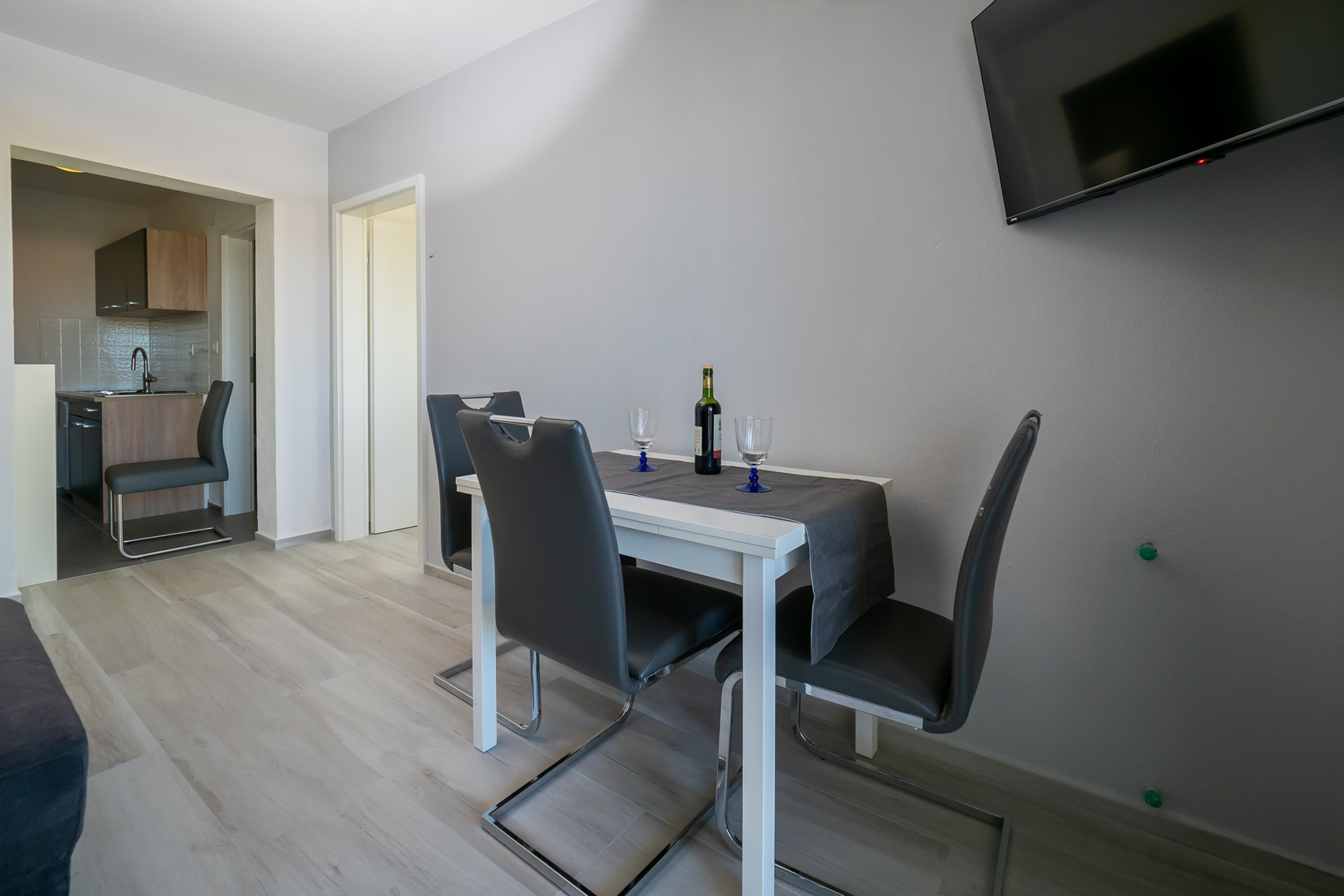 A modern dining area with a white table, black chairs, and a TV mounted on the wall.