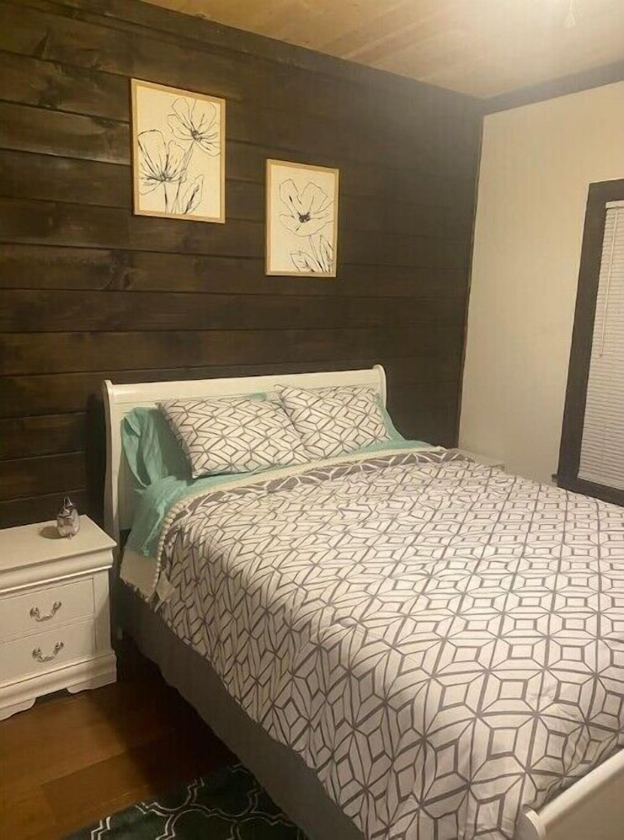 Un dormitorio con una cama, una mesita de noche y dos obras de arte colgadas en la pared.