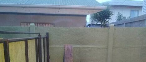 A brick-built outdoor grill area enclosed by a yellow wall and a metal gate.