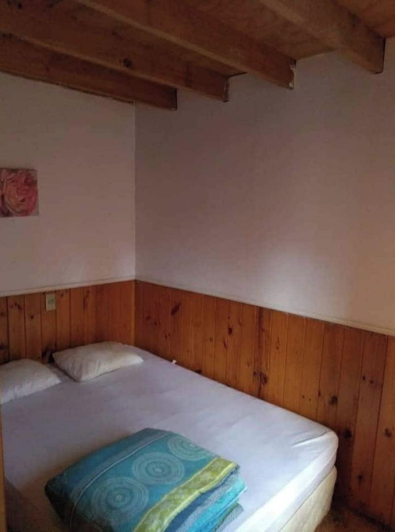 Una cama individual con cabecera de madera en una habitación con paredes blancas y techo de madera.