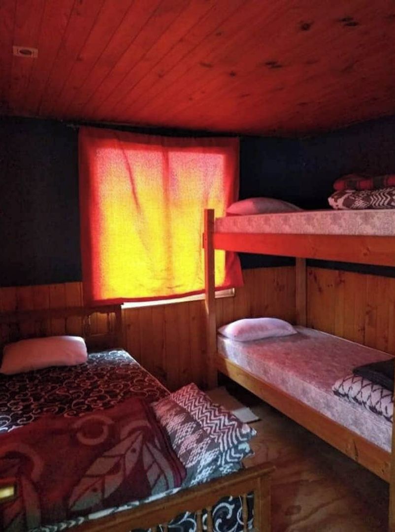 Une chambre avec un lit superposé, un plafond et des murs en bois, une fenêtre avec des rideaux rouges et une couvre-lit à motifs.