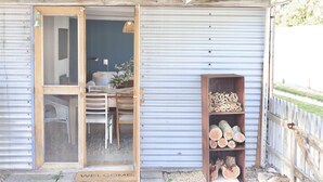 A rustic wooden door leading into a room with a chair and a table, a metal door, and a shelf with wood logs. - MAISIES ROBE - WI-FI - DOG FRIENDLY (Robe)