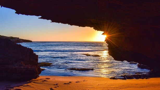 A sunset view through a cave opening with ocean waves and footprints on the sand. - MAISIES ROBE - WI-FI - DOG FRIENDLY (Robe)