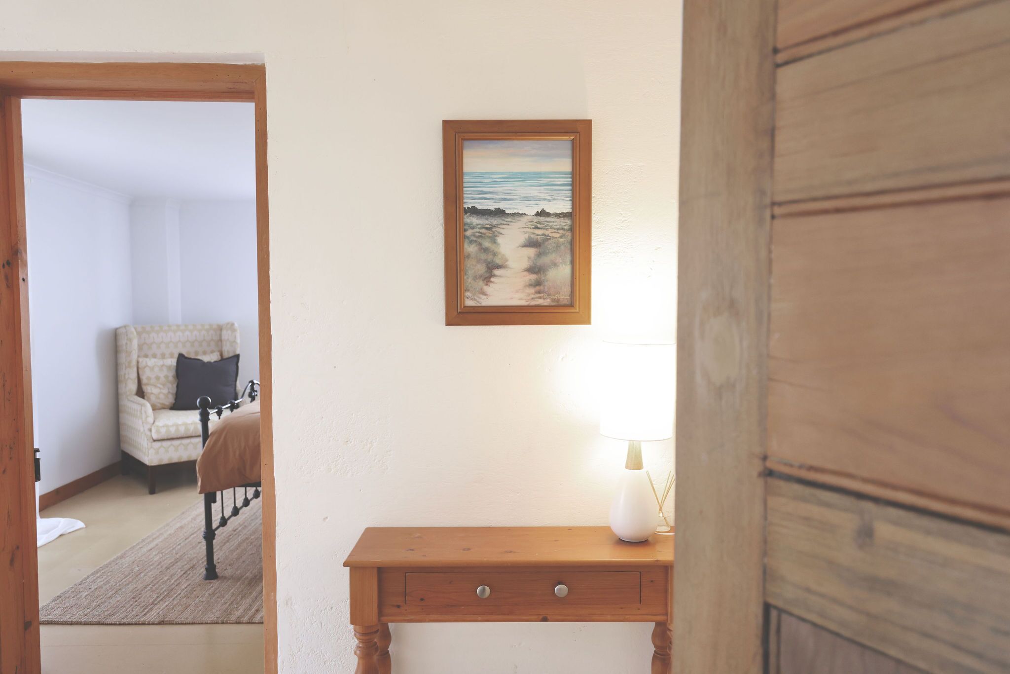 Ein Schlafzimmer mit einem Bett, einem Nachttisch, einer Lampe und einem Bild von einer Strandlandschaft.
