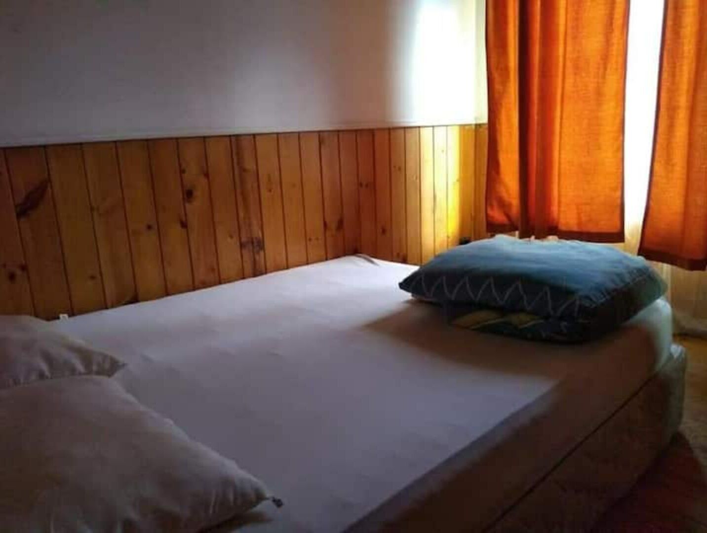A single bed with a wooden headboard, a pillow, and a blue pillow on the bed.