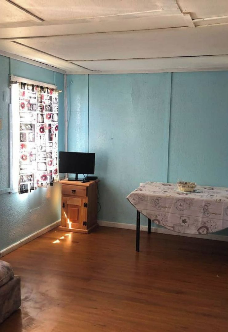 A room with a wooden cabinet, a table with a patterned tablecloth, and a window with a floral curtain.