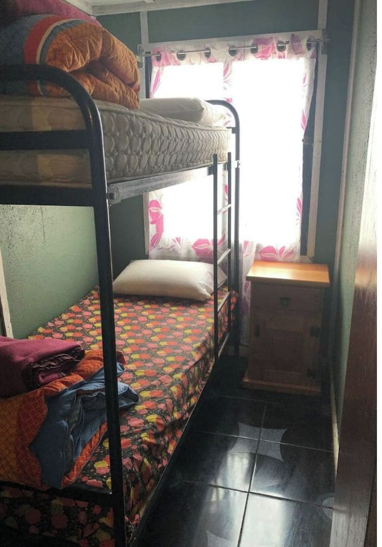 A bunk bed room with a small wooden cabinet and a window with curtains.