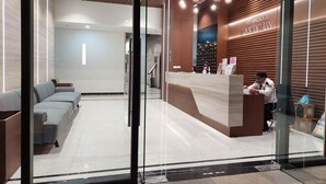 Zona de recepción con un mostrador de madera, un área de estar con sofás y un panel de vidrio.