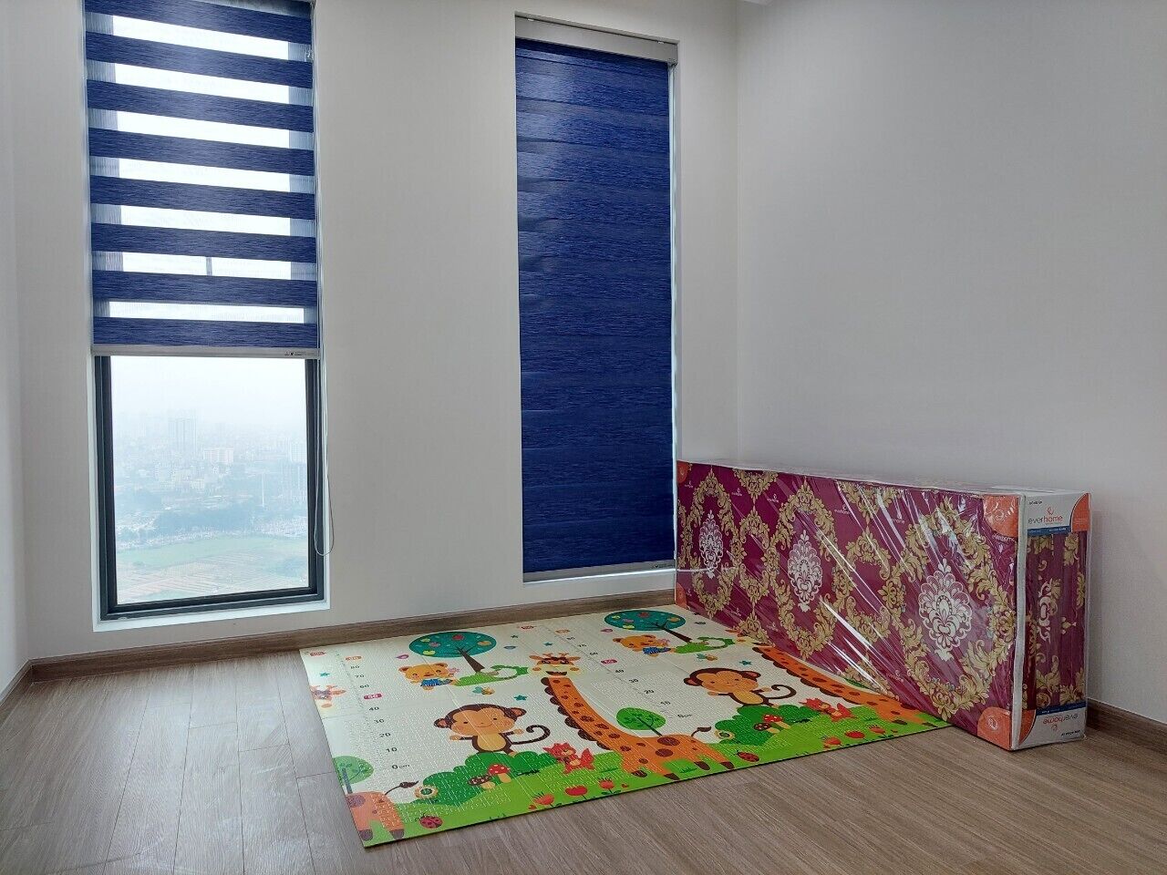 Een kamer met een groot raam, een blauwe schuifdeur, een kleurrijke speelmat en een gedeeltelijk zichtbaar meubelstuk.