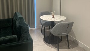 A modern living room with a dark green sofa, a round table with two chairs, and a large mirror on the wall.